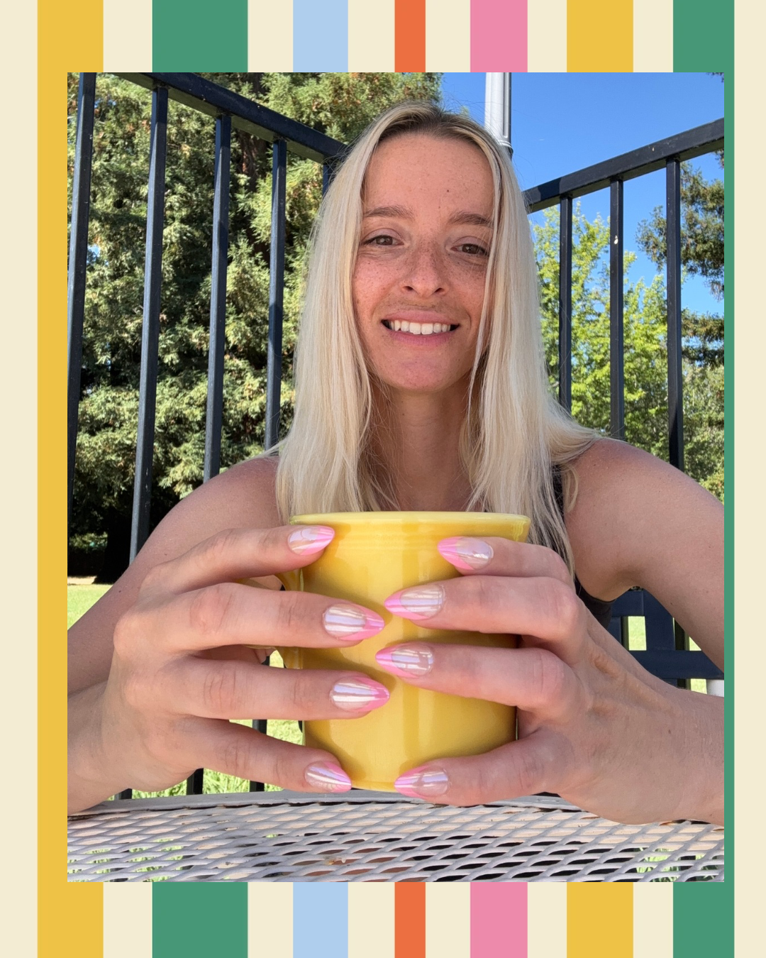 A smiling blonde woman outdoors holding a bright yellow ceramic mug with both hands, framed by a colorful striped border.